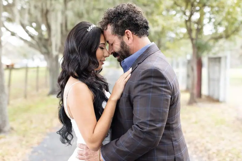 A bride and groom rest their foreheads together under trees hung with Spanish moss