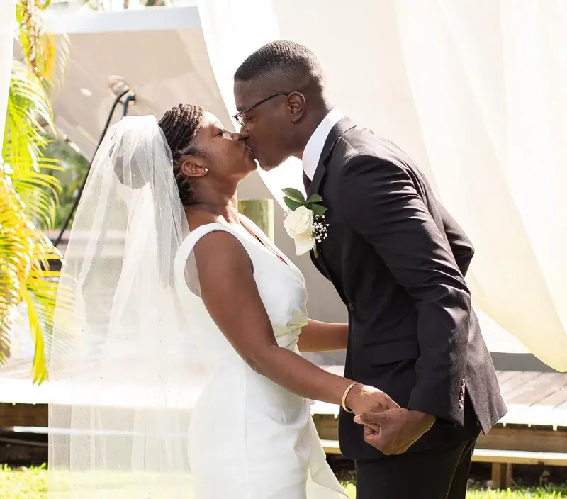 A bride in a long veil and her groom kiss beneath sheer white drapes