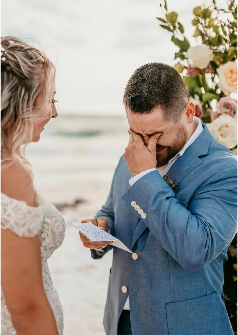 A groom wipes away tears as he reads his vows to the bride at a beach ceremony