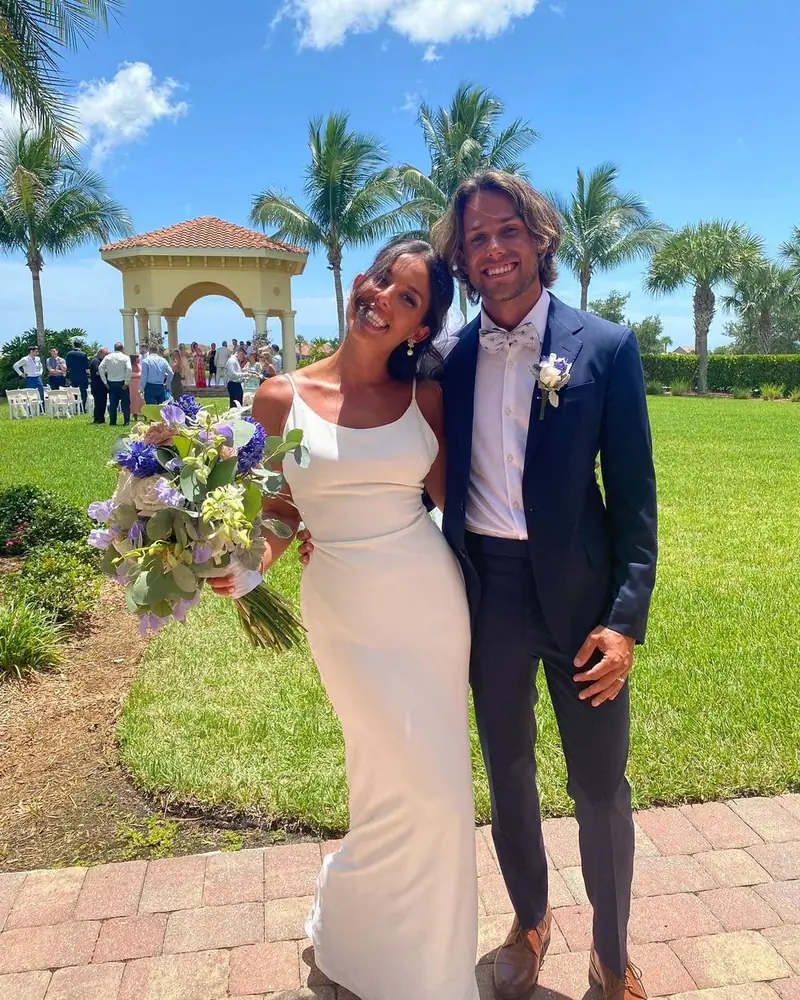 A smiling couple on a sunny lawn, a gazebo and palm trees behind them