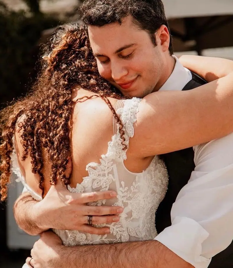 A groom hugs his bride tightly, eyes closed and smiling