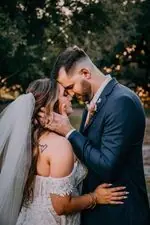 A bride and groom touch foreheads under trees at dusk