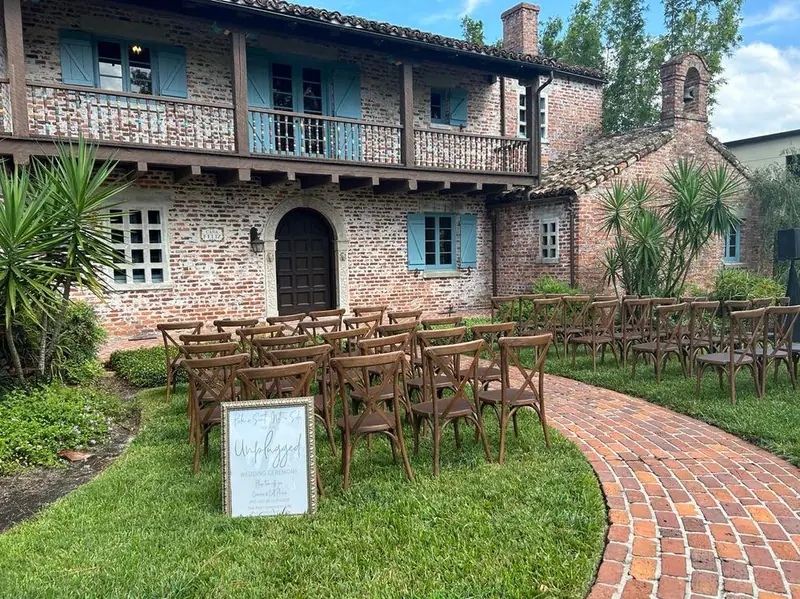 Wooden chairs set in rows for a garden ceremony beside a brick building with blue shutters