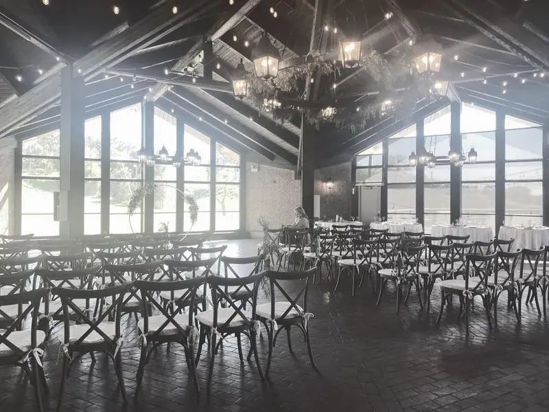 Black-and-white photo of a ceremony room set with rows of cross-back chairs and tall windows