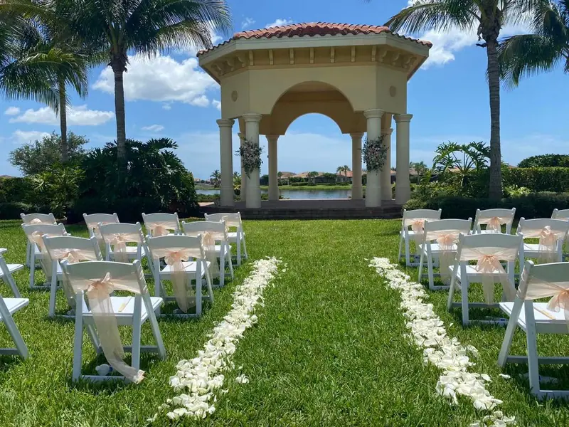 Rows of white chairs with blush sashes face a gazebo, the aisle lined with white petals