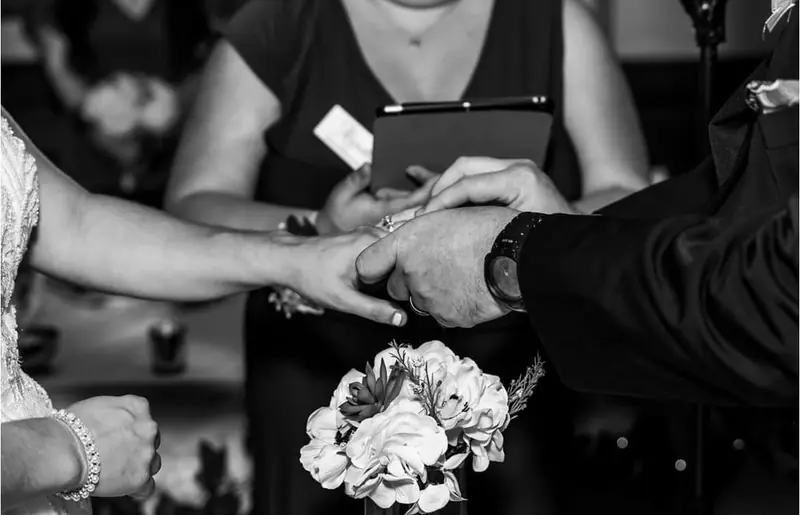 Black-and-white close-up of the couple's hands during the ring exchange, a corsage in front