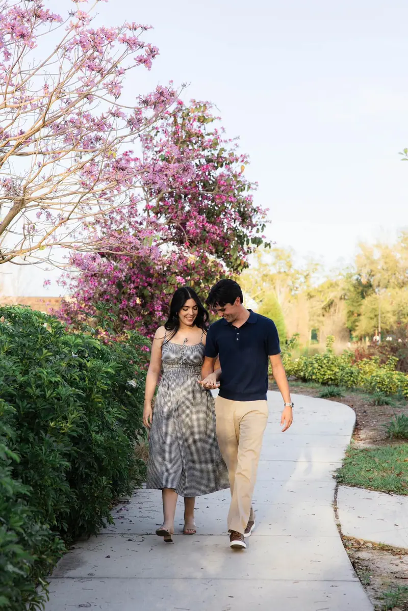 A couple walks along a garden path under a tree in pink bloom